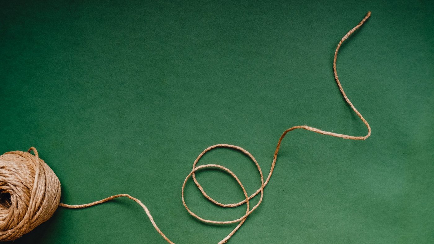 A ball of twine with a loose strand looping and then stretching out smoothly across a green background