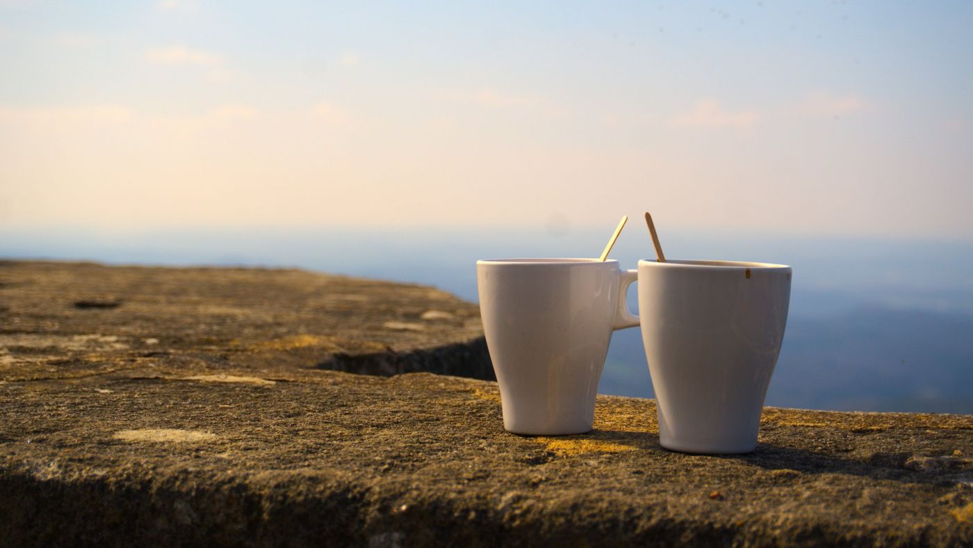 Two white mugs side by side on a stone wall, with a soft evening sky behind